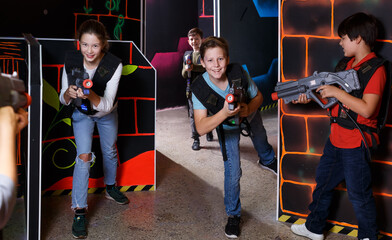 Happy teens aiming laser guns at other players during lasertag game in dark room