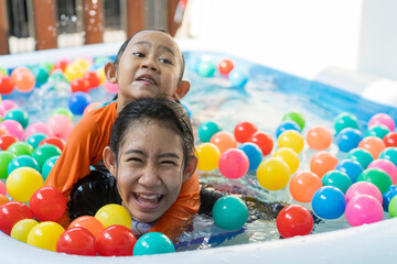 Fototapeta na wymiar Asian young sisters playing in the swimming pool at home and colored balls