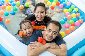 Fototapeta na wymiar Asian happy family father and daughter playing in the swimming pool at home, and coloured balls