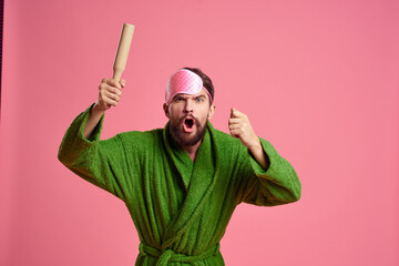 Portrait of a man in a pink sleep mask and a wooden rolling pin emotions green robe irritability model