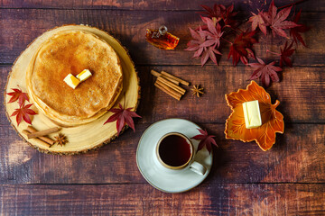 Thin Russian pancakes (crepes) with maple syrup and tea on a wooden table. Leaves, anise stars and cinnamon sticks are placed on the board as decoration. Autumn atmosphere.