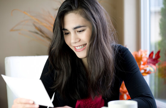 Teenage girl or young woman happily reading note in hand