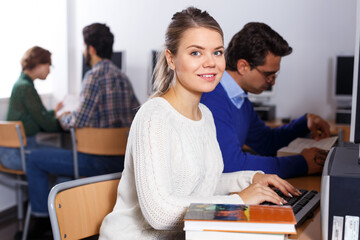 Portrait of young female student working with computer and books in university library
