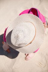 Young girl wearing a broad brim safe sun hat pink jumper jacket playing in the sand at the beach on a bright summer day 