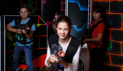 Emotional teen girl with laser pistol playing laser tag with friends on dark labyrinth