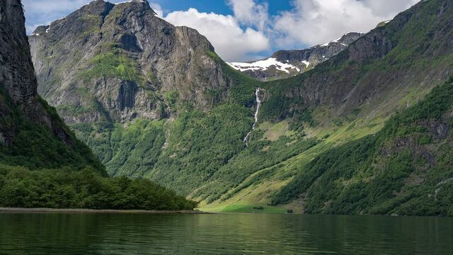 Kayaking in the Naeroyfjord, Norway. High mountains, covered with lush forest, rising above the fjord. Water is calm and mirrorlike reflecting passing clouds and the green mountainsides.