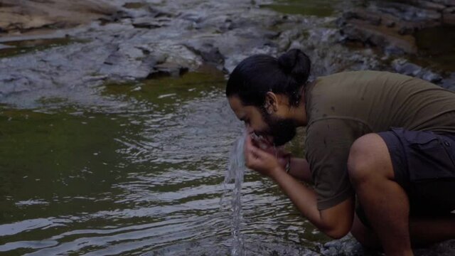 vivek bearded long hair man washing face in fresh water in jungle water .