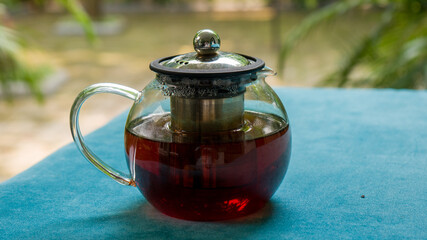 A transparent pot of tea, photographed at close range with green colored fabric underneath and blurred background.