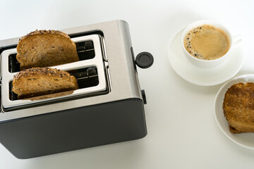 Toaster with multi-grain bread and a cup of black coffee on white background