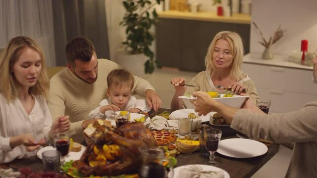 People sitting at dining table taking tasty boiled sweet corn while celebrating Thanksgiving day together