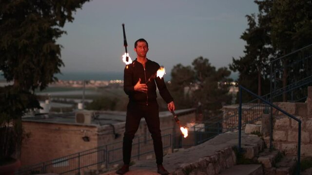 Professional juggler performing juggling tricks with 3 fire clubs, outdoors at sunrise. Slow motion wide angle shot.