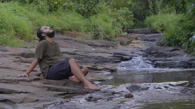 vivek bearded long hair man rlaxing on river stone  in jungle water