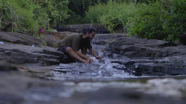 vivek bearded long hair man rlaxing on river stone  in jungle