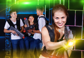 Fototapeta na wymiar Portrait of exciting positive glad girl with laser pistol playing laser tag in dark room