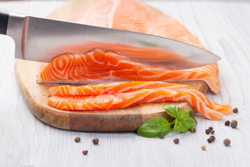 Knife cuts slices of fresh raw salmon
