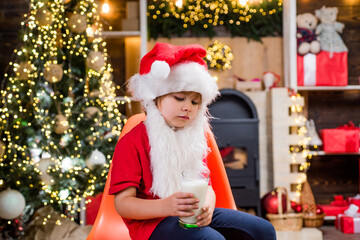 Fototapeta na wymiar Portrait of Santa Claus Drinking milk from glass and holding cookies. Happy Santa Claus - little child boy with glass of milk and cookie. Christmas Beard style.
