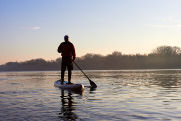 Water tourists is paddling on SUP (Stand up paddle board) at Danube river at sunrise in early morning