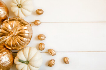 Fototapeta na wymiar Pumpkins and nuts painted in gold on a white wooden background. Flat layout with space for text