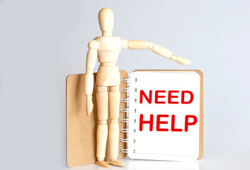 Wooden man shows with a hand to white notepad with text Need help