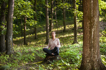 Naklejka na ściany i meble Young woman wearing yoga pants meditating in the woods on a sunny morning.