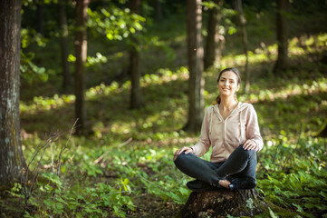 Young woman wearing yoga pants meditating in the woods on a sunny morning.