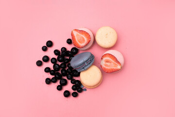 Obraz na płótnie Canvas five macaroons of different colors are laid out in a circle and decorated with strawberries and blueberries on a pink background, top view