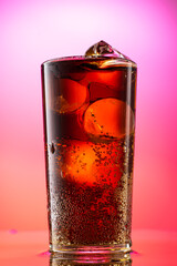 pour cola into a glass with pieces of pure real ice on a red purple gradient background