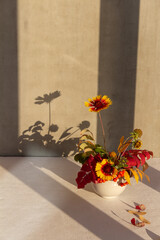 Autumn yellow-red leaves and flowers in a light ceramic vase on a light background
