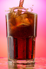 pour cola into a glass with pieces of pure real ice on a red purple gradient background