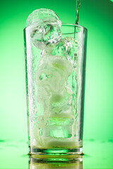 pouring green tarragon lemonade into glass with pieces of pure real ice on green gradient background