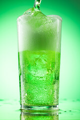 pouring green tarragon lemonade into glass with pieces of pure real ice on green gradient background