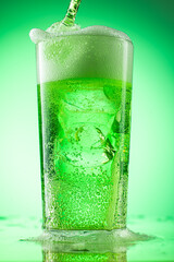 pouring green tarragon lemonade into glass with pieces of pure real ice on green gradient background