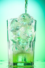 pouring green tarragon lemonade into glass with pieces of pure real ice on green gradient background