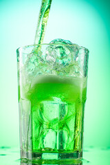 pouring green tarragon lemonade into glass with pieces of pure real ice on green gradient background