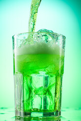pouring green tarragon lemonade into glass with pieces of pure real ice on green gradient background