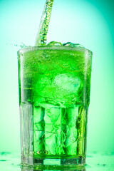pouring green tarragon lemonade into glass with pieces of pure real ice on green gradient background