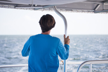 caucasian man blue shirt behind boat ocean blue sky travel sea looking