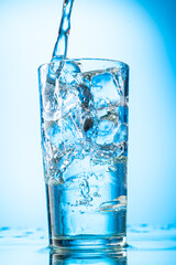 pour clear water into a glass with chunks of pure real ice on a blue gradient background