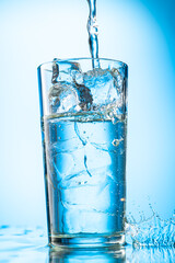 pour clear water into a glass with chunks of pure real ice on a blue gradient background