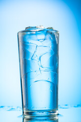 pour clear water into a glass with chunks of pure real ice on a blue gradient background
