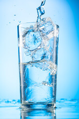 pour clear water into a glass with chunks of pure real ice on a blue gradient background