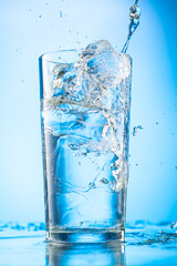 pour clear water into a glass with chunks of pure real ice on a blue gradient background