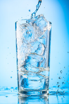 pour clear water into a glass with chunks of pure real ice on a blue gradient background