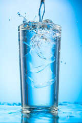 pour clear water into a glass with chunks of pure real ice on a blue gradient background