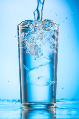 pour clear water into a glass with chunks of pure real ice on a blue gradient background