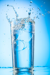 pour clear water into a glass with chunks of pure real ice on a blue gradient background