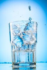 pour clear water into a glass with chunks of pure real ice on a blue gradient background