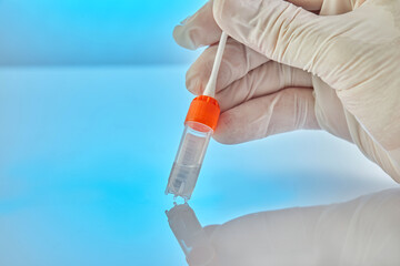 DNA test. Test tube with liquid for DNA analysis and a gloved hand holding a stick on a blue background with reflection