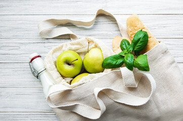Fresh apples, milk and bread in eco cotton bag on a white wooden table