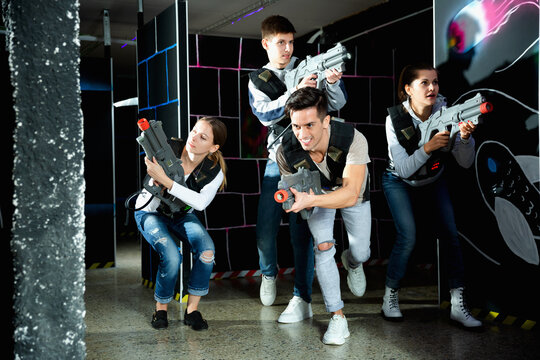 Modern satisfied cheerful smiling young people with laser pistols playing laser tag on dark labyrinth